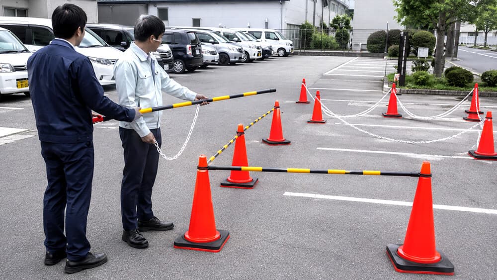 駐車場でプラチェーンとコーンバーを比較する安全用品担当者